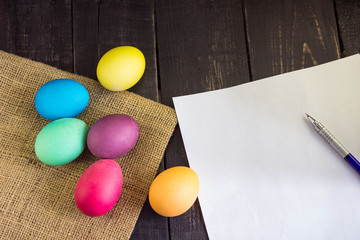 Fototapeta na wymiar Colorful easter eggs with blank paper and pen on rustic wooden table . Ready to write a letter