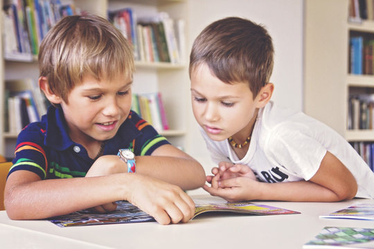 Smiling school kids sitting and reading book in library - Powered by Adobe