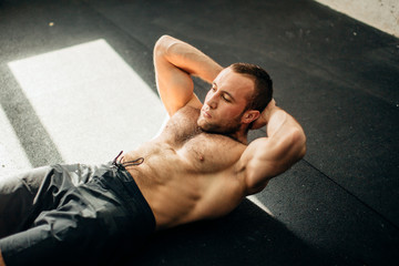Male fitness model doing sit ups and crunches exercising abdominal muscles, six pack visible wearing no shirt - obrazy, fototapety, plakaty