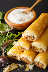 Filo rolls briouats with meat, eggs and greens close-up and yogurt. vertical