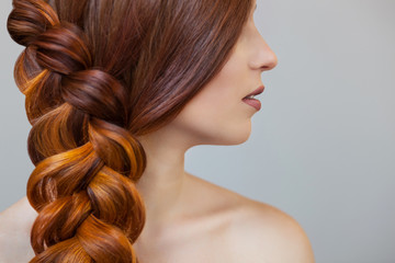 Beautiful girl with long red hair, braided with a French braid, in a beauty salon. Professional...