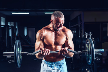 Muscular bodybuilder guy doing exercises on biceps with big dumbbell in gym