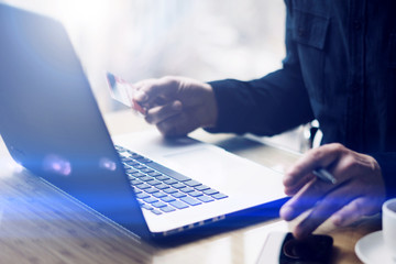 Closeup view of businessman working at the wooden table at modern loft office.Man holding credit card hand and using smartphone.Blurred background.Horizontal,visual effects.