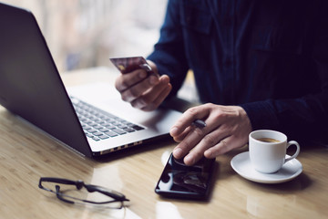 Businessman holding credit card in hand and using smartphone,laptop computer at the wooden table.Blurred background.Horizontal.
