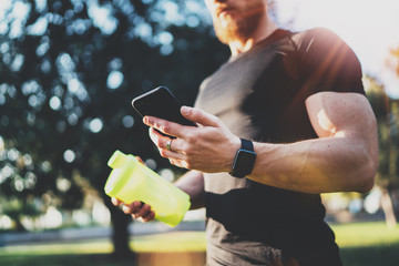 Workout smart fitness concept.Young Muscular athlete checking training programm on smartphone application after perfect workout session at sunny morning.Blurred background.