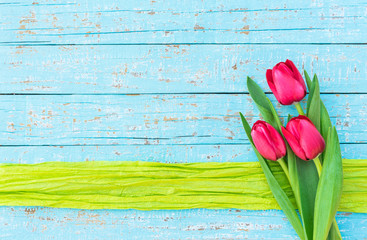 Fototapeta na wymiar Frühling Blumen Strauss Tulpen pink auf Holz Hintergrund blau mit Geschenkband grün
