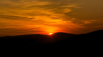 Obraz premium The sky is magenta and orange with alpenglow and clouds. Abstract red orange sky. Dramatic orange sky at the sunset background. The sundown behind hills.