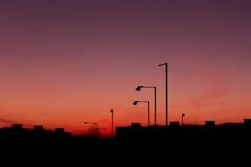 Silhouette of buildings and streetlights in city before sundown.  The sky is red and purple with...