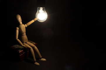 New idea concept. The wooden man and burning light bulb, isolated on black background. 