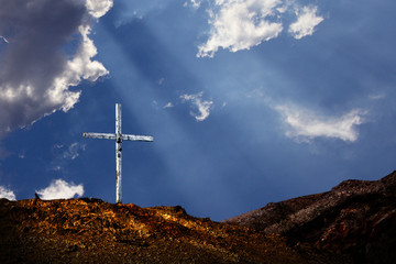 Renewal: Single white cross on a lone hill, with cloudy blue sky and rays of sun in the background. Ideal for seasonal advertising, poster, or greetings card applications.