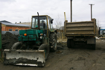 An old Soviet tractor digs and loads waste stone processing near the shop