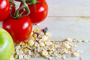 Foods for healthy eating: tomatoes, apple, cereal on light wood background