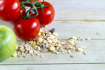 Foods for healthy eating: tomatoes, apple, cereal on light wood background