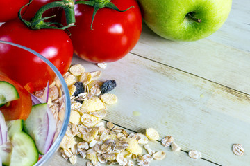 Foods for healthy eating: tomatoes, apple, cereal, salad on light wood background