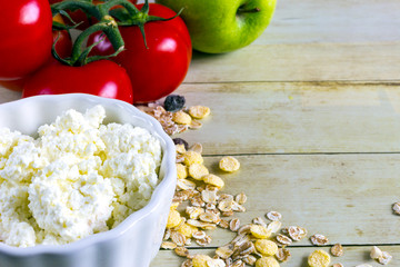 Foods for healthy eating: cottage chesse, tomatoes, apple, cereal on light wood background