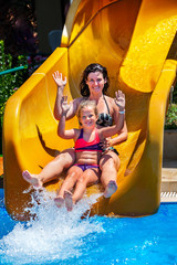 Swimming pool slides for family with children on water slide at aquapark . Kid with mother holiday outdoor. Girl and woman hands up in aqua park. Flowing water with people in summer water park . - 142136060