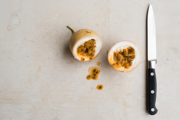 High angle view of panama gold passionfruit in halves with knife to right on cream limestone background