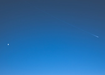 aircraft condensation strip on blue sky and moon.