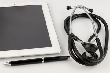 Tablet computer, metal silver-black pen and stethoscope on a white background