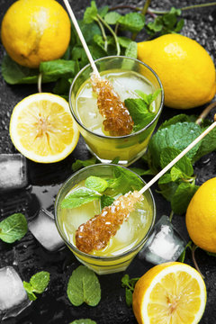 Fresh mojitos cocktails with lemons, fresh mint, ice cubes and sugar sticks on wooden background