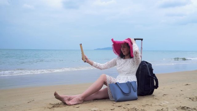 Girl seats on the beach with her bagage and ipad