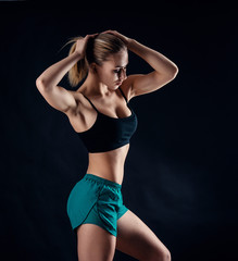 Sporty young girl in sportswear showing muscles on black background. Tanned young athletic woman. A great sport female body.