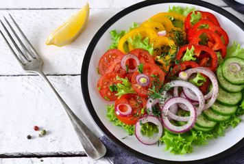 Vegetable mix salad with avocado and olive oil sauce on a white, wooden background.