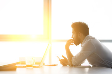 Toned of businessman waiting for interview while sitting at table and looking at window. Handsome...