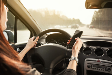 girl with red hair at the wheel of a car in her hands is holding a phone.