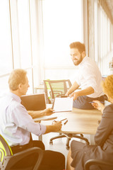 Toned of handsome businessman sitting on table in office and giving his CV to employees. Business...