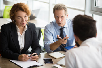 Happy HR specialists of company taking interview. People communicating with young man and asking him to tell about his previous experience.