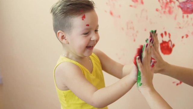 Young mother with her little boy are lmixing colors at their hands yo leave beautiful handprints on the wall. Mother and child concept. Slowmotion.
