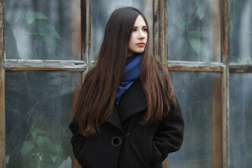 Young beautiful girl in a black coat and blue scarf for a posing in the autumn / spring park. An elegant brunette girl with gorgeous extra long hair. Lifestyle concept.
