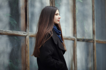 Young beautiful girl in a black coat and blue scarf for a posing in the autumn / spring park. An elegant brunette girl with gorgeous extra long hair. Lifestyle concept.