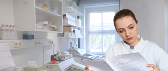  Young female scientist reading printed notes in scientific laboratory, panoramic image