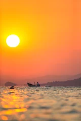 Zelfklevend Fotobehang Fisherboat on Chapala Lake in Mexico with white pelican flying into the sunrise with orange and pink illuminated sky and mountains in the background © Martin Rudlof