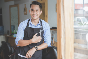 young barber expert  with hair clipper smiling looking at camera in barbershop