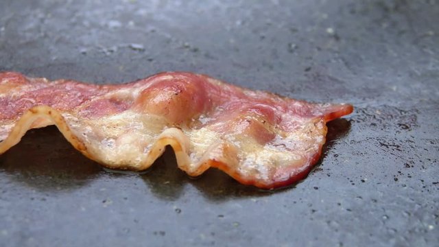 Close-up of a slice of bacon lays on the hot grill