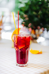 Red cocktail with straws and orange wedge in high glass