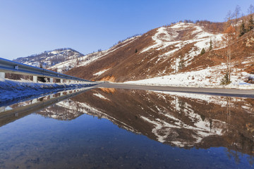 The mountain near the road is reflected in the spring puddle of water