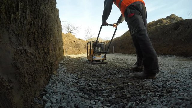 The man at the construction site.
Man serving compacting machine. Stone compaction during the construction of a private swimming pool.
