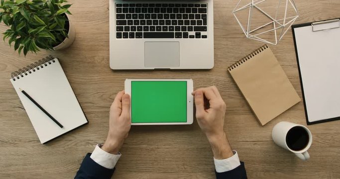 Business man using tablet, scrolling, checking information on tablet with green screen. Hands top view. Office desk background. Slow motion. red epic