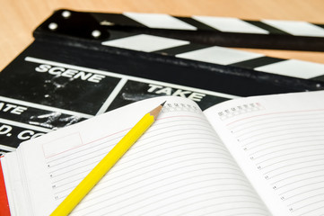 Movie clapper with notepad and pen on wooden table