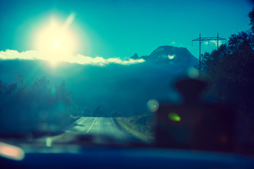 Driving a car on mountain road. Sky with sun dusk. Nature Norway. Polar circle. View through windscreen