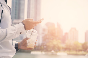 Confident young businessman in a suit standing outdoors and holding phone in his hands in the background, business use smart phone and social media.