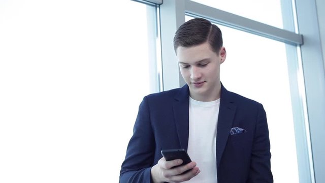 Good News From Friends in Social Networks/Close up of a young businessman checking his social networks during the break. He is in the office with large bright windows. Copy space