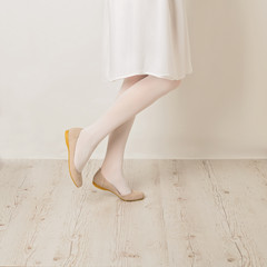 Female legs in white tights, skirt and ballet flats on a white background.