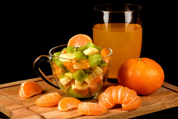 Fruit salad and segments of tangerine on a black background.