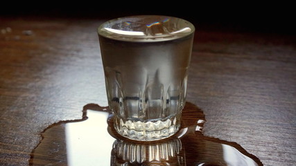 Crowded glass of vodka on a wooden table. Part of vodka drain side.