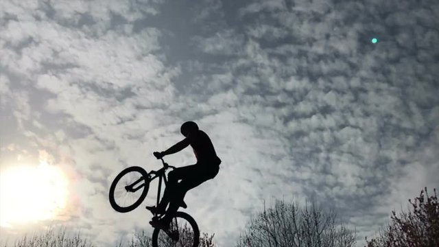Boy riding a bike performing a trick in silhouette against sunset sky, in slow motion.